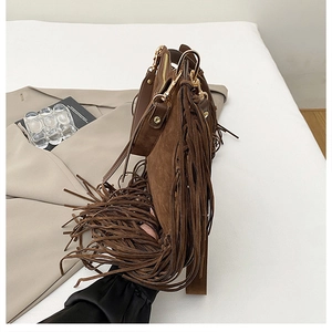 Close-up of brown suede shoulder bag featuring long fringe tassels and golden metal hardware