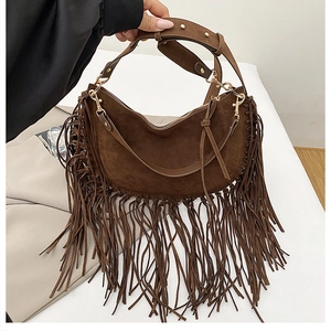 Macro detail of dark brown suede crescent bag featuring long fringe and gold stud hardware