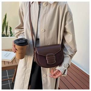 Detail of a brown leather saddle bag with white contrast stitching and adjustable strap