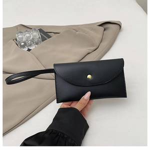 Detail of minimalist black clutch bag with golden metal buckle and wristlet strap