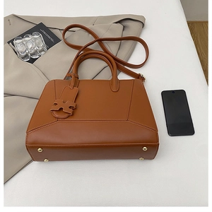 Close-up of caramel brown tote bag featuring H-shaped charm and metallic bottom studs