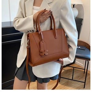 Detail of a brown leather tote bag with geometric stitching and an H-shaped charm accessory