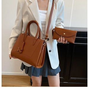 Detail of a brown leather tote and envelope clutch set with an H-shaped metallic tag
