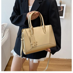 Detail of a metallic gold handbag featuring a unique H-shaped charm and detachable strap