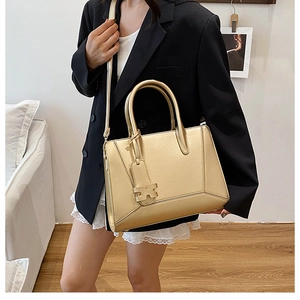 Detail of golden tote bag with H-shaped metallic charm and detachable shoulder strap