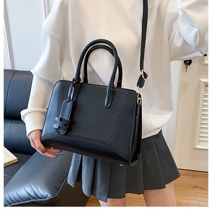 Close-up of black leather tote with adjustable strap and decorative H-letter charm