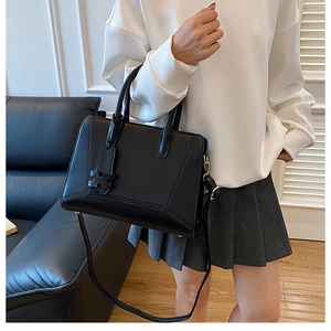 Detail of matte black leather tote bag featuring dual handles and a geometric charm tag