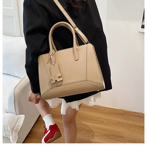 Close-up of beige faux leather handbag with H-pendant and adjustable shoulder strap