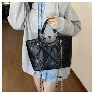 Detail of black quilted tote bag featuring gold chain strap and large diamond stitching