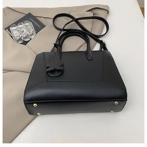 Detail view of black leather handbag featuring protective gold feet and adjustable strap