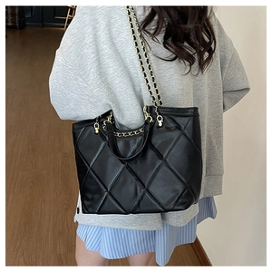 Close-up of black quilted leather tote bag with gold chain strap on a model shoulder