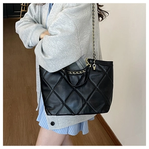 Detail of a black quilted tote bag featuring a metal chain strap and spacious side profile