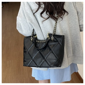 Close-up of black quilted leather tote bag with elegant gold chain shoulder strap