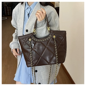 Detail of brown quilted tote bag with golden chain strap and leather handle
