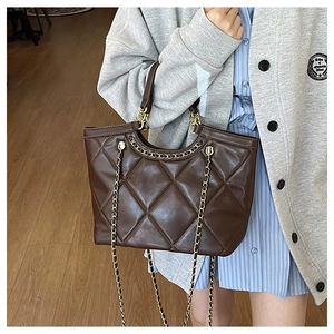 Detail of dark brown quilted tote bag with polished leather finish and gold chain strap