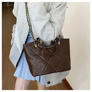 Detailed close-up of brown quilted handbag with woven gold chain strap on female model