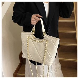 Detail of cream quilted tote bag with gold chain strap on a stylish woman