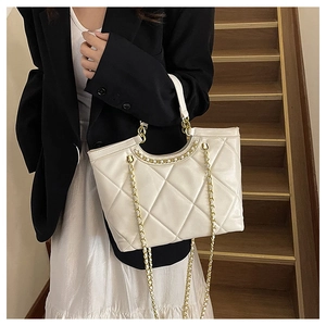 Detail shot of a cream quilted tote bag with gold chain strap on a wooden staircase