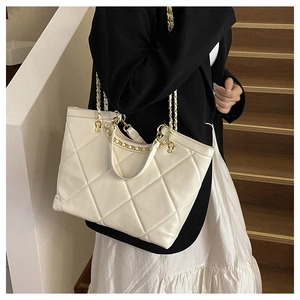 Detail of white quilted tote bag featuring gold chain strap and large capacity texture