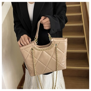 Macro detail of beige quilted tote bag featuring gold chain strap and luxury texture