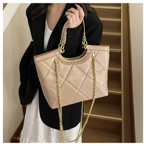 Detailed shot of beige quilted tote bag with chain strap on model's shoulder for commute