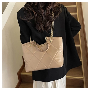Close-up of beige quilted tote bag with gold chain strap worn over a black blazer