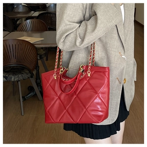 Detail of red quilted tote bag featuring golden chain straps for commuter style