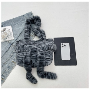 Flat lay view of a striped fuzzy shoulder bag next to a mobile phone for size reference