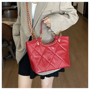 Detail of red quilted tote bag styled with beige blazer and golden chain strap