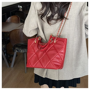 Fashionable red quilted tote bag with gold chain strap carried by a model in a cafe setting