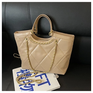 Detailed close-up of a beige quilted chain tote bag with gold hardware on a leather sofa