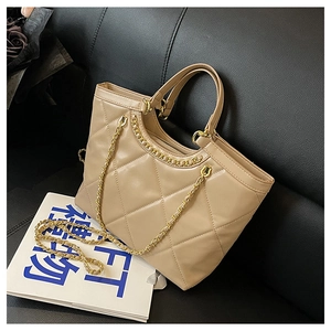 Detail of apricot quilted tote bag with golden chain strap on a black leather sofa