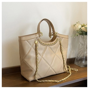 Detail of beige quilted tote bag with gold chain strap on a wooden shelf in a cozy room