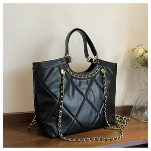 Detail view of a black quilted tote bag with gold chain strap in a cozy home setting