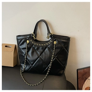 Detailed close-up of a black quilted tote bag with gold chain strap and dual handles