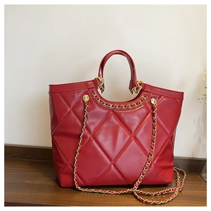 Close-up of red quilted leather tote bag with gold chain strap on a wooden surface