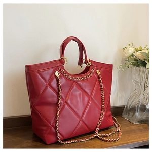 Detail of red quilted tote bag with golden chain strap on a dark wooden table surface