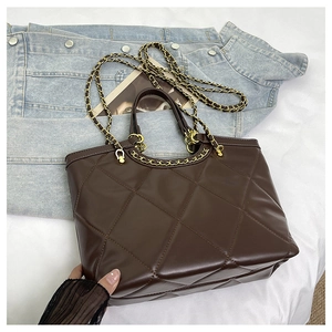 Detail of dark brown quilted tote bag with polished gold chain strap and texture