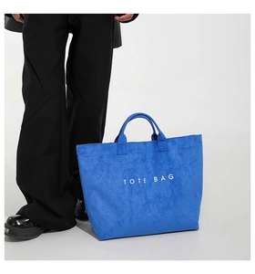 Detail of blue suede tote bag featuring a spacious interior and white printed text