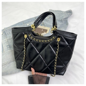 Detail of black quilted leather handbag with gold chain strap on white bedding