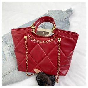 Detail of red quilted tote bag featuring golden chain strap and synthetic leather texture