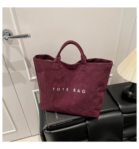 Detail of burgundy faux suede tote bag with white TOTE BAG text in a minimalist setting