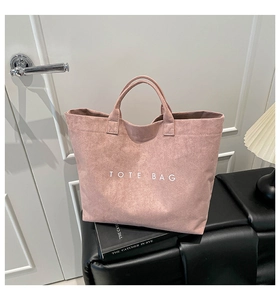 Detail of dusty rose suede tote bag with white lettering on a black bench