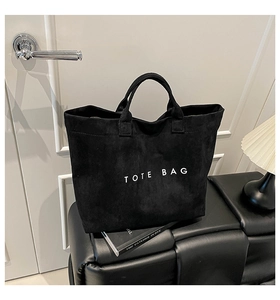 Detail of minimalist black suede tote bag with white slogen print on a leather bench