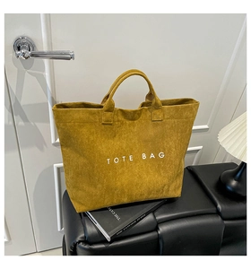 Close-up of a mustard yellow suede tote bag featuring a minimalist white logo print