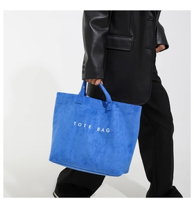 Detail of bright blue suede tote bag with white TOTE BAG print and velvet texture