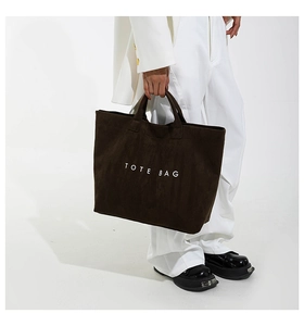 Detail of large dark brown suede tote bag held by model with white suit outfit