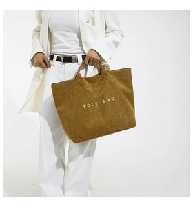 Detail of a brown corduroy tote bag with TOTE BAG text print shown on a white suit model