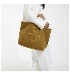Brown suede tote bag with white text held by model in white suit on plain background