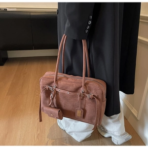 Close-up of brown suede tote bag featuring adjustable metal buckles and mini bag accessory